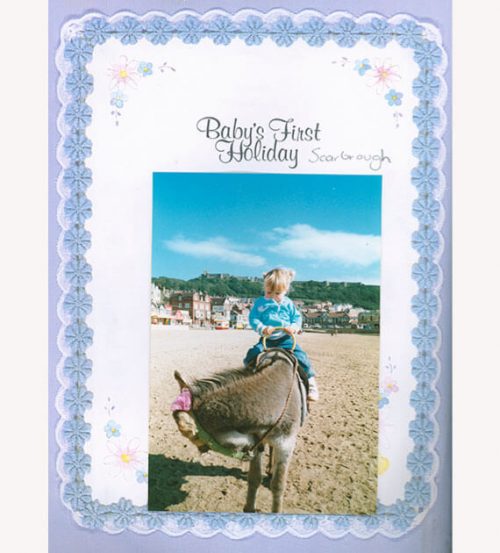 Baby scrapbook reading "Baby's first Holiday" featuring little girl riding a donkey on the beach